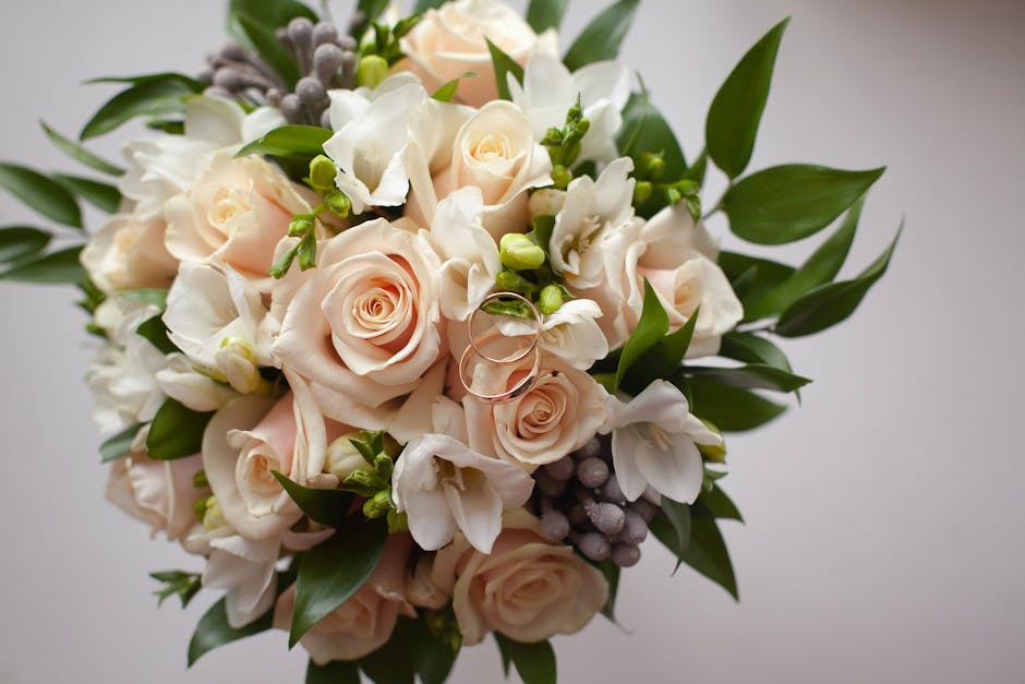 A close-up view of a floral bouquet arranged with pale pink roses, white orchids, and green foliage, accented with small purple berries. The roses and orchids have fresh, soft petals and are gathered