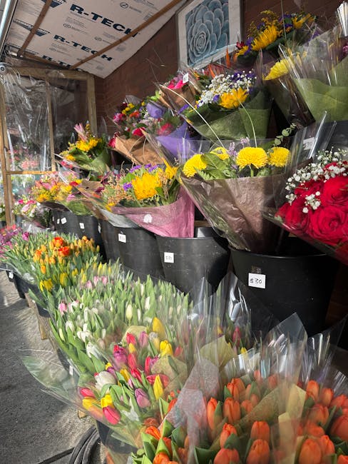 A variety of fresh flower bouquets displayed in black plastic containers inside a flower shop, showing vibrant colors and diverse types of flowers including yellow chrysanthemums, pink and white tulip